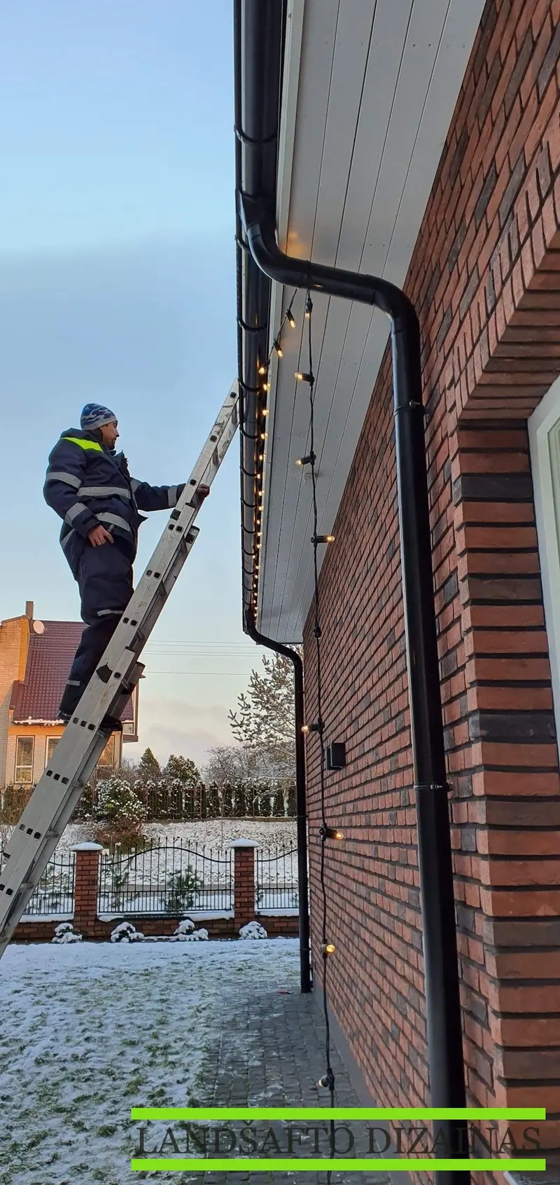 Montuotojas ant kopėčių tvirtina girliandą po latakais